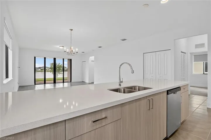 Kitchen featuring light brown cabinetry, open floor plan, light tile patterned floors, light stone counters, and stainless steel dishwasher