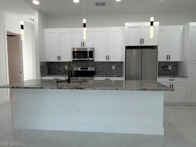 Kitchen with appliances with stainless steel finishes, hanging light fixtures, backsplash, dark stone countertops, and recessed lighting