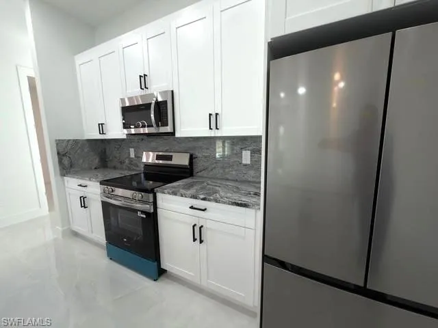 Kitchen with stainless steel appliances, dark stone countertops, white cabinets, and tasteful backsplash