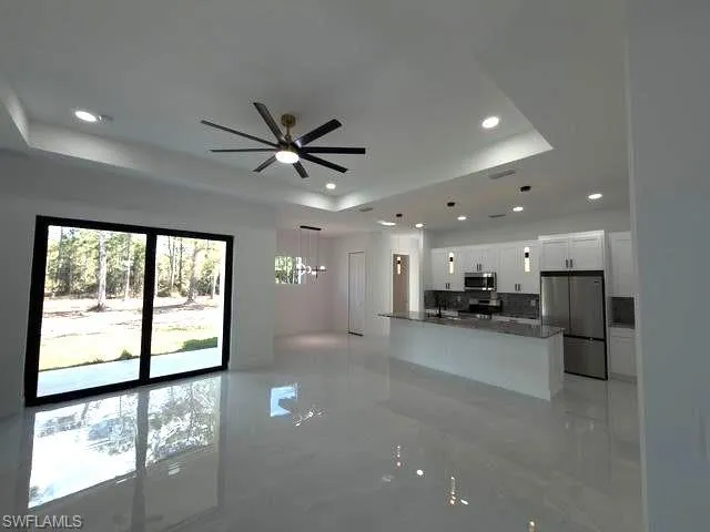 Unfurnished living room featuring a raised ceiling, recessed lighting, and a ceiling fan
