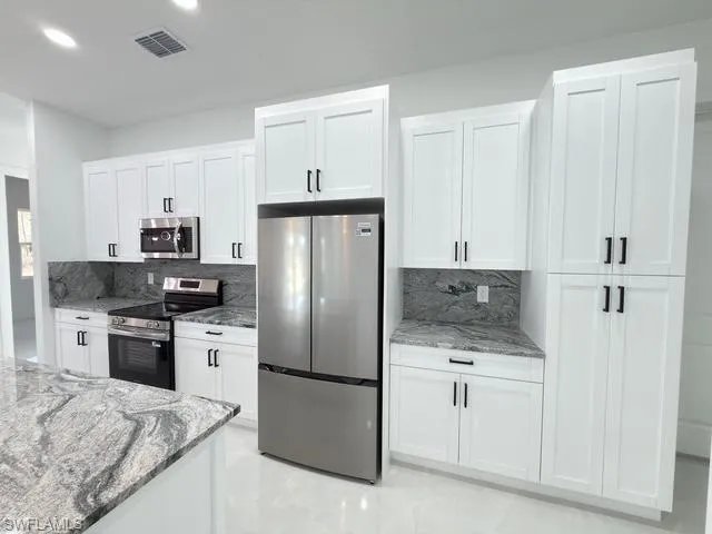 Kitchen featuring light stone countertops, appliances with stainless steel finishes, white cabinetry, and recessed lighting