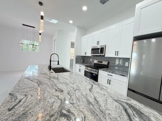 Kitchen featuring light stone counters, appliances with stainless steel finishes, white cabinets, decorative backsplash, and recessed lighting