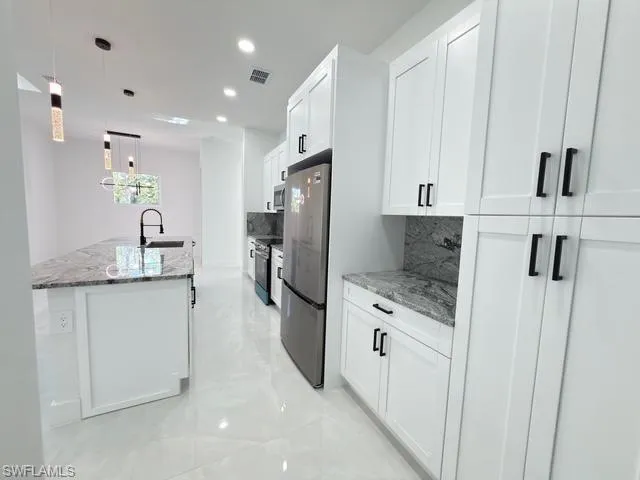 Kitchen with hanging light fixtures, light stone countertops, decorative backsplash, white cabinetry, and recessed lighting