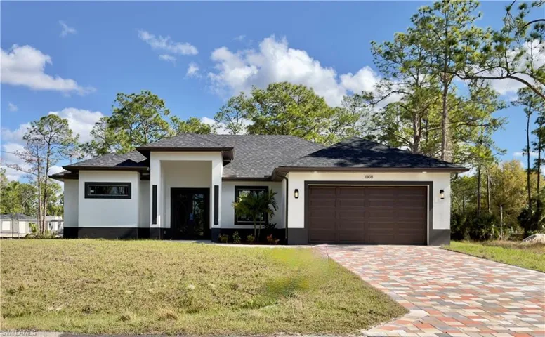 Prairie-style home featuring stucco siding, roof with shingles, decorative driveway, a front yard, and an attached garage