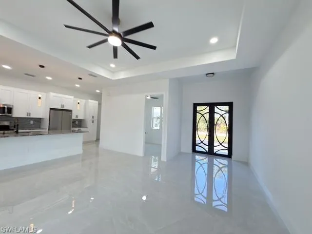 Unfurnished living room featuring light marble finish flooring, a ceiling fan, a tray ceiling, french doors, and recessed lighting