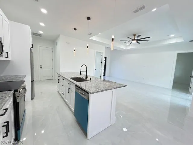 Kitchen with decorative light fixtures, white cabinetry, light stone counters, a tray ceiling, and range with electric stovetop