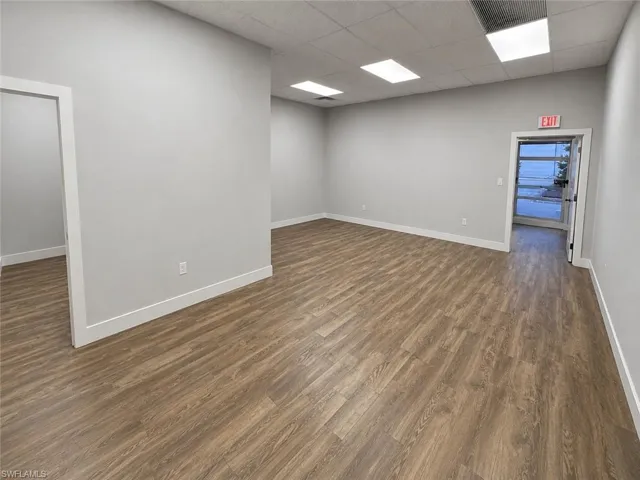 Open-concept interior featuring wood-finish flooring, light gray walls, white baseboards, and a dropped ceiling with recessed lighting