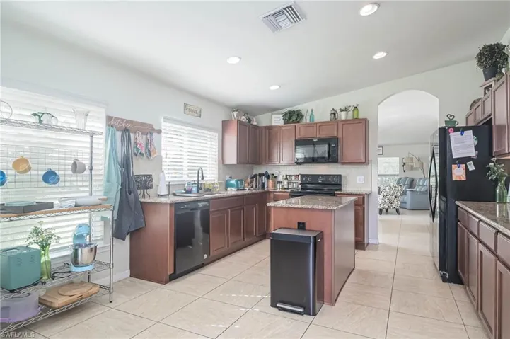 Kitchen featuring a kitchen island, light stone counters, black appliances, and tasteful backsplash