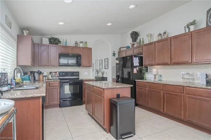 Kitchen with sink, black appliances, light tile patterned floors, a center island, and vaulted ceiling