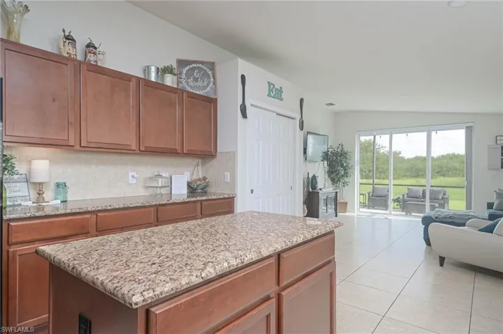 Kitchen with light stone countertops, vaulted ceiling, tasteful backsplash, a kitchen island, and light tile patterned floors