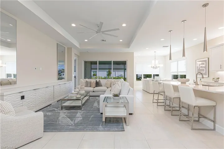 Tiled living room with ceiling fan with notable chandelier, a raised ceiling, and sink