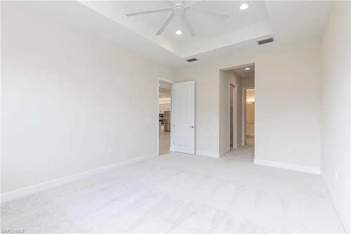Unfurnished bedroom with ensuite bathroom, a raised ceiling, light colored carpet, and ceiling fan