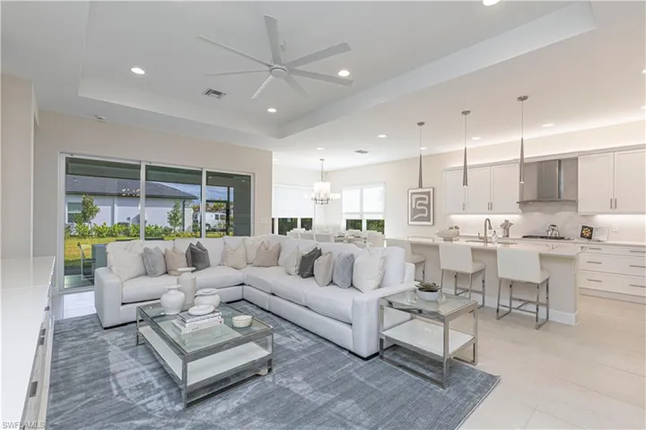 Tiled living room featuring a tray ceiling, sink, and ceiling fan with notable chandelier