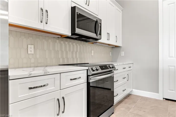 Kitchen featuring stainless steel appliances, tasteful backsplash, white cabinets, light stone counters, and light tile patterned flooring