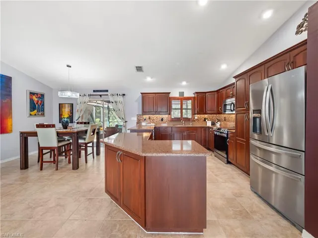 Kitchen with stainless steel appliances, vaulted ceiling, light stone countertops, tasteful backsplash, and plenty of natural light