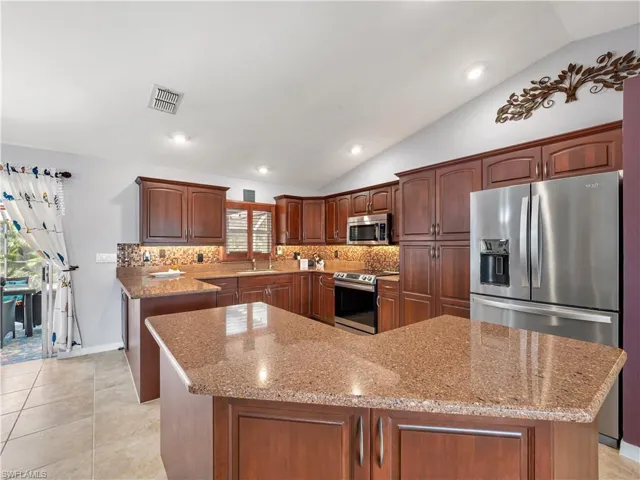 Kitchen featuring stainless steel appliances, vaulted ceiling, light stone counters, recessed lighting, and backsplash