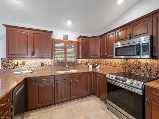 Kitchen featuring stainless steel appliances, lofted ceiling, backsplash, light stone counters, and dark wood finish cabinets