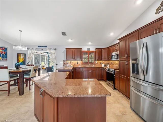Kitchen featuring lofted ceiling, stainless steel appliances, light stone countertops, decorative backsplash, and a kitchen island