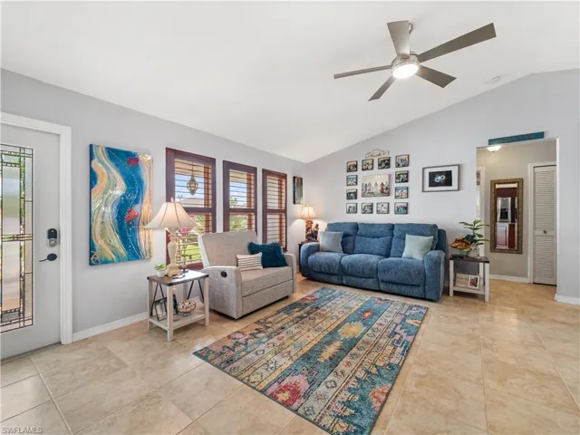 Living room with a ceiling fan, lofted ceiling, and light tile patterned flooring