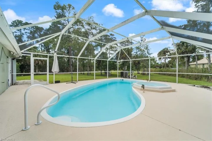 Outdoor pool with glass enclosure, a sunroom, a patio, and a lawn