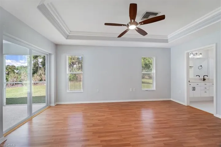 Unfurnished bedroom featuring access to outside, a raised ceiling, light wood-style flooring, crown molding, and ensuite bath