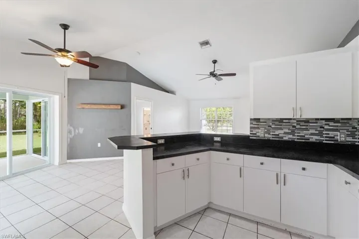 Kitchen with a ceiling fan, white cabinets, vaulted ceiling, light tile patterned flooring, and decorative backsplash