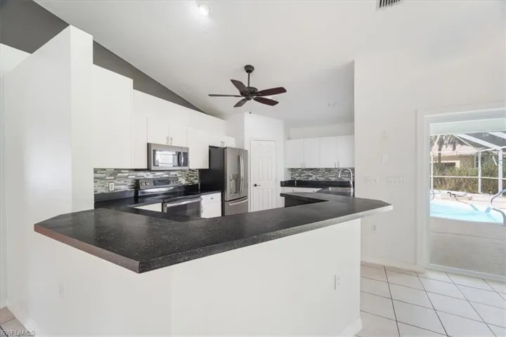 Kitchen with tasteful backsplash, light tile patterned floors, stainless steel appliances, a peninsula, and lofted ceiling