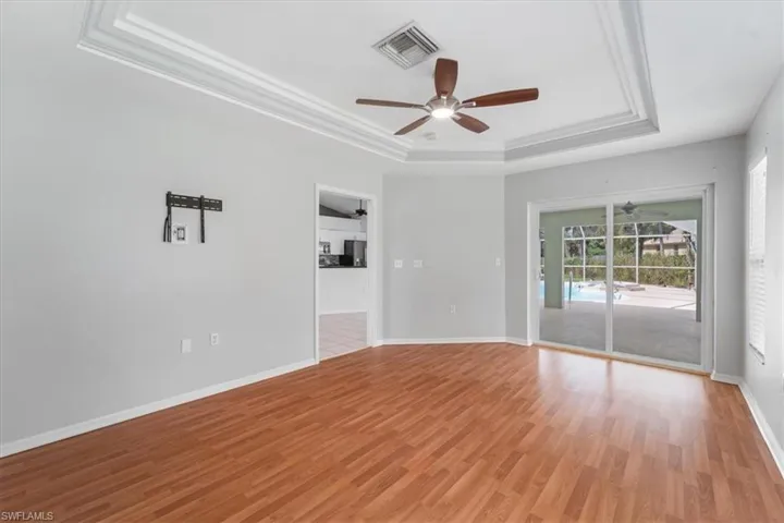 Empty room featuring a raised ceiling, light wood-style flooring, ornamental molding, and a ceiling fan
