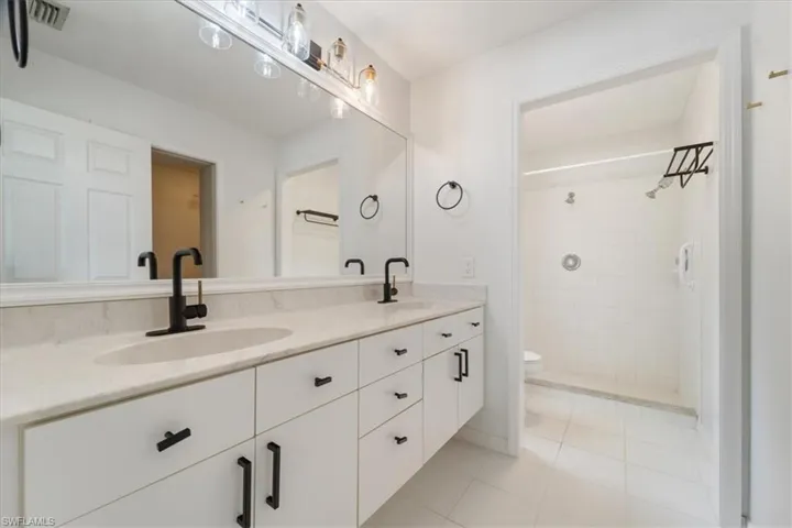 Bathroom with double vanity, light tile patterned floors, and a tile shower