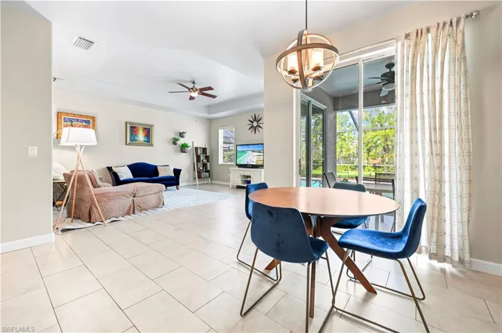 Dining room featuring ceiling fan with notable chandelier, a tray ceiling, and light tile flooring
