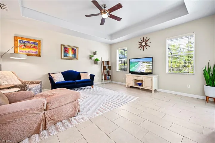 Living room featuring a tray ceiling, light tile flooring, and ceiling fan
