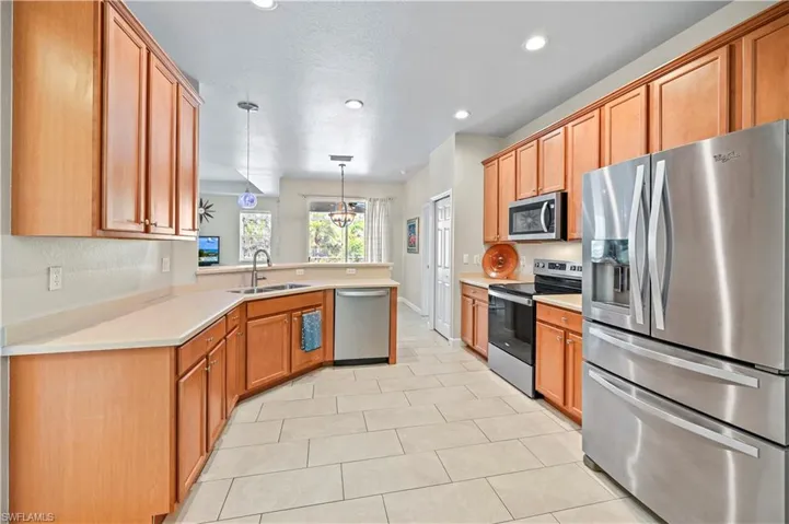 Kitchen with stainless steel appliances, kitchen peninsula, decorative light fixtures, sink, and light tile flooring