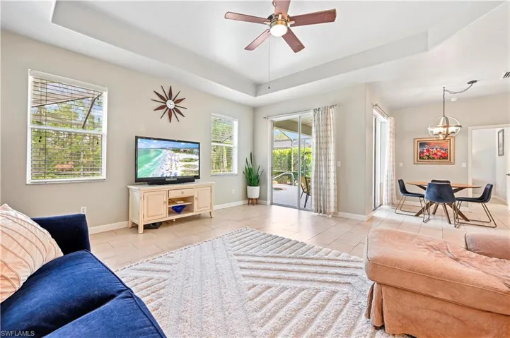 Living room with a raised ceiling, ceiling fan with notable chandelier, and light tile floors