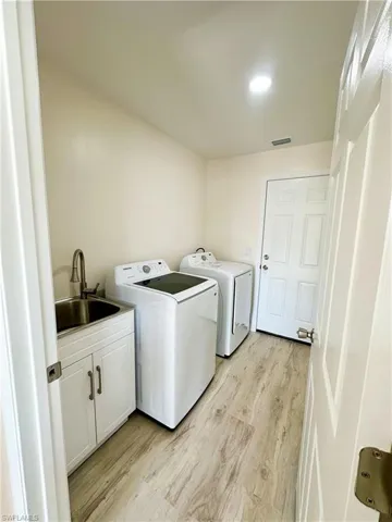 Clothes washing area with washing machine and clothes dryer, light hardwood / wood-style floors, cabinets, and sink