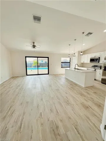 Unfurnished living room with ceiling fan, light wood-type flooring, sink, and lofted ceiling