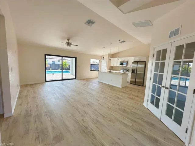 Unfurnished living room featuring french doors, light wood-type flooring, vaulted ceiling, ceiling fan, and sink