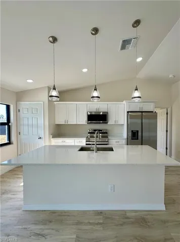 Kitchen featuring decorative light fixtures, light stone counters, white cabinetry, and stainless steel appliances