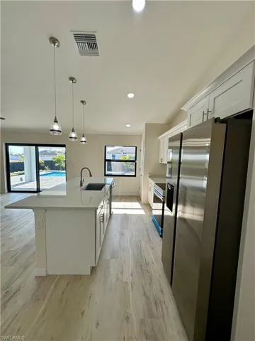 Kitchen featuring sink, pendant lighting, a center island with sink, stainless steel fridge with ice dispenser, and white cabinetry