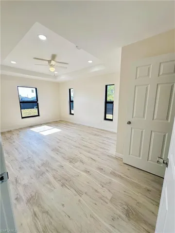 Spare room with a raised ceiling, ceiling fan, plenty of natural light, and light wood-type flooring
