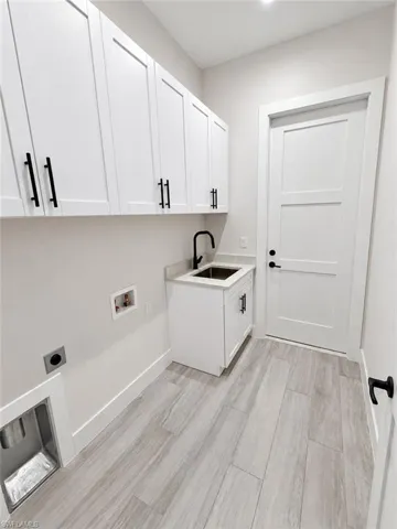 Utility room with extensive white cabinetry, a single-basin sink with a matte black faucet, and light wood-finish flooring