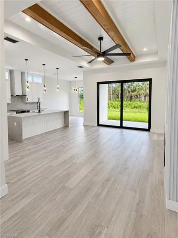 Expansive open-concept living area featuring wood-finish flooring, a tray ceiling with wood beams, and a modern ceiling fan