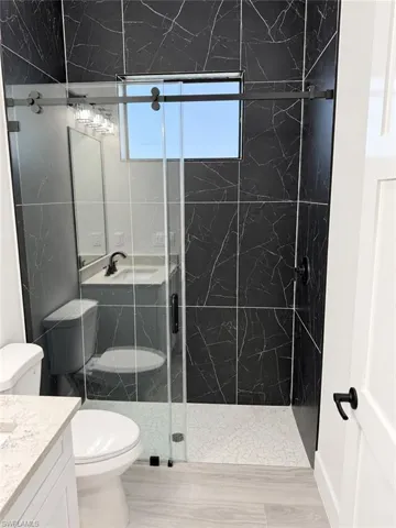 Walk-in shower with clear glass enclosure, black-veined wall tile, and light-toned shower floor tile