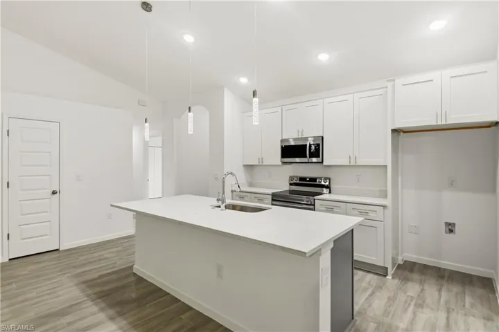 Kitchen with stainless steel appliances, white cabinetry, a kitchen island with sink, light wood-style floors, and lofted ceiling
