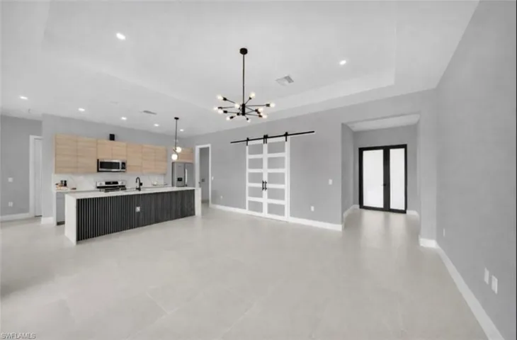 Kitchen featuring a barn door, open floor plan, a large island with sink, a chandelier, and hanging light fixtures