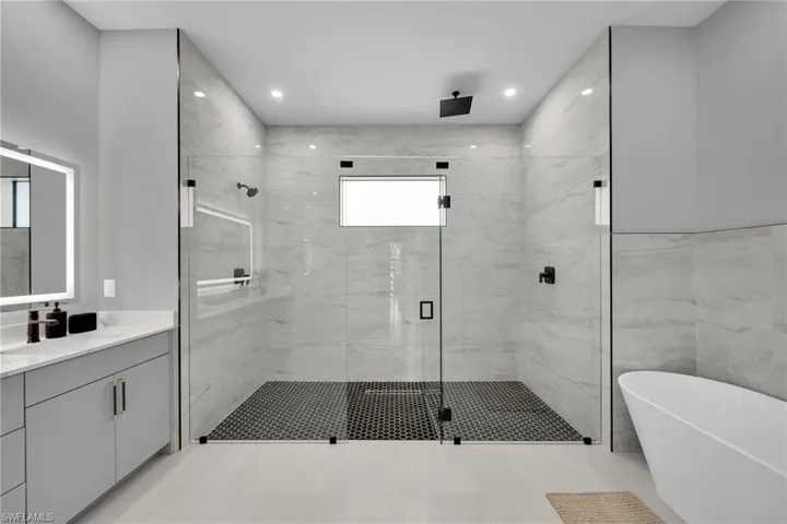 Bathroom with a freestanding tub, a marble finish shower, vanity, and recessed lighting