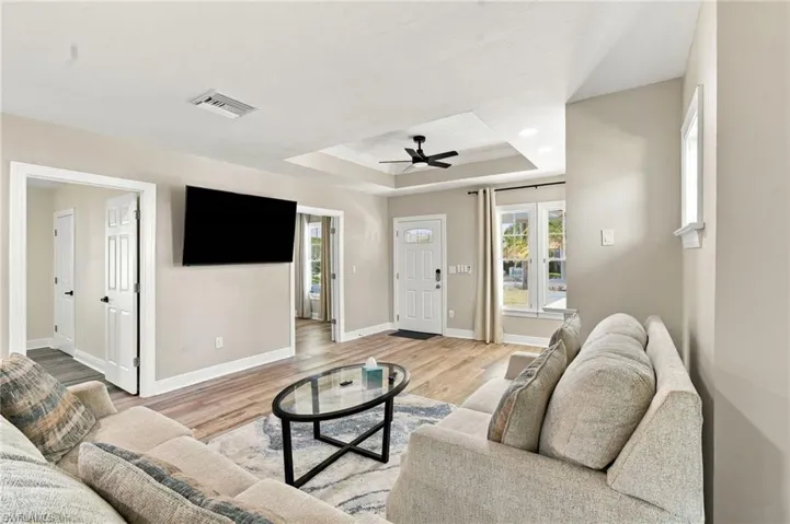 Spacious living area featuring wood-finish flooring, a tray ceiling with a ceiling fan, and recessed lighting, as well as flat screen TV.