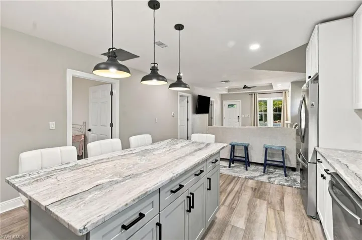 Kitchen featuring an expansive island with a stone countertop, pendant lighting, light gray cabinetry, and wood-finish flooring