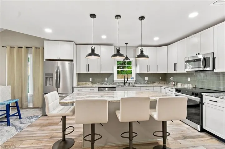 Kitchen featuring white cabinetry, a center island with countertop seating, stainless steel appliances, a tile backsplash, and wood-finish flooring