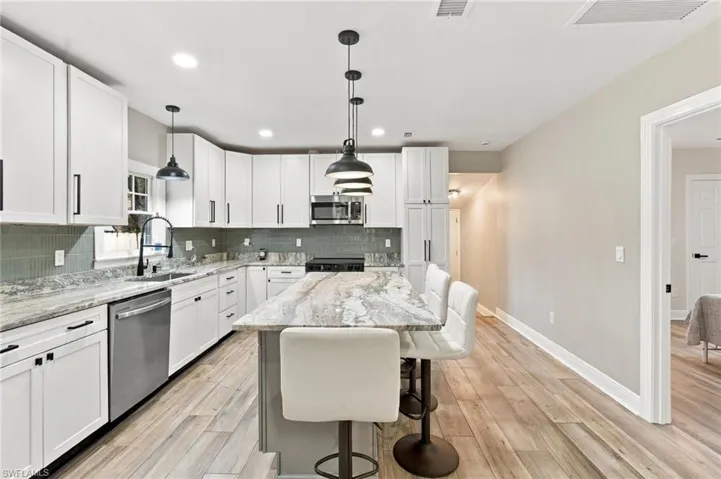 Modern kitchen featuring white shaker cabinetry, patterned stone countertops, stainless steel appliances, and wood-finish flooring