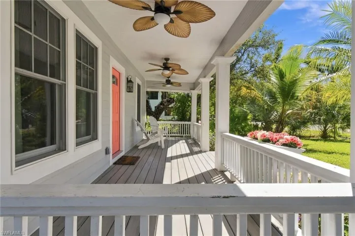 Expansive front porch featuring multiple ceiling fans, plank flooring, a white railing, and a vibrant entry door
